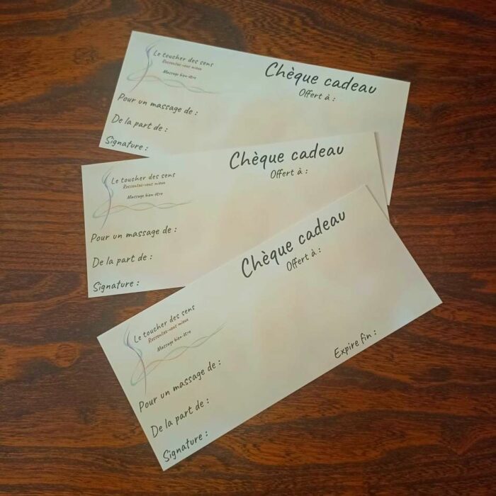 Trois chèques-cadeaux pour offrir un massage qui sont posés sur une belle table en chêne massif.