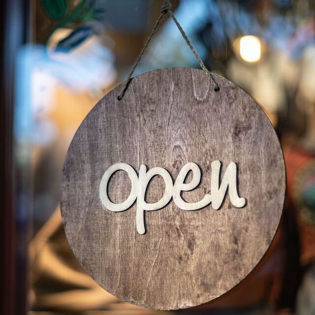 Pancarte en bois ronde accrochée devant une vitre avec de la ficelle avec écrit "open" dessus.