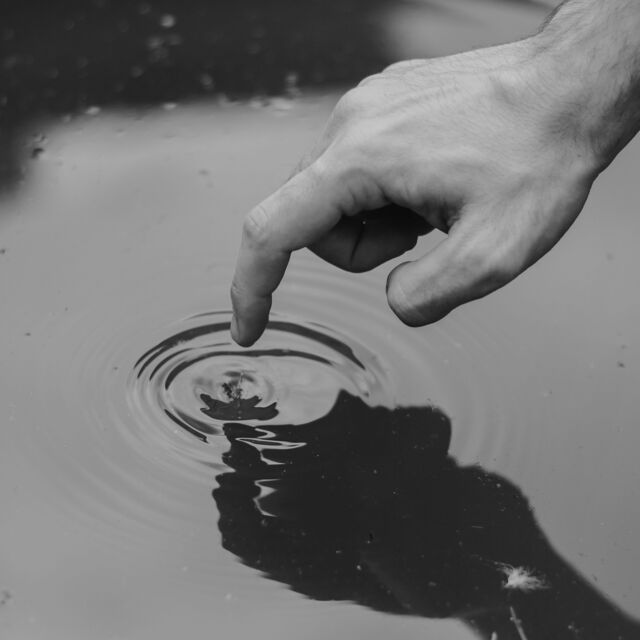 Main droite avec index déplié qui vient toucher la surface de l'eau d'un lac, créant ainsi une belle onde sur l'eau.